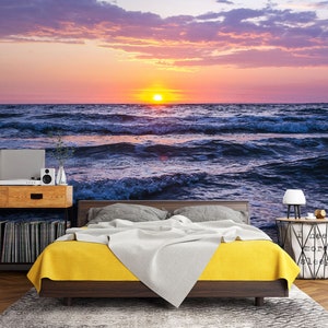 May include: A bedroom with a bed with a yellow and white comforter. The wall behind the bed is a mural of a sunset over the ocean.