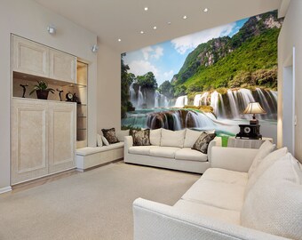 May include: A living room interior with a large wall mural depicting a lush green waterfall cascading down a mountainside. The room features a white sofa, a side table with a lamp, and a large cabinet with shelves.