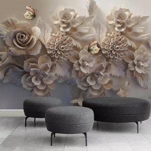 May include: Three round grey fabric ottomans with black metal legs in front of a wall with a 3D floral design. The floral design is white and beige and features a variety of flowers and leaves.