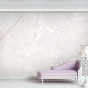 May include: A white chaise lounge with a light purple cushion sits in front of a white marble wall with pink veins. A white lamp with a white lampshade is on the right side of the image.