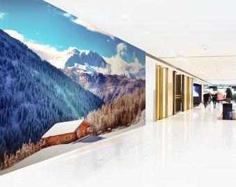 May include: A snowy mountain scene with a small wooden cabin in the foreground. The scene is printed on a large wall mural in a modern shopping mall.