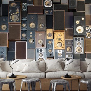 May include: A wall covered in vintage speakers of various sizes and colors. The speakers are arranged in a random pattern, creating a unique and eclectic look. The wall is a light gray color, and the speakers are a mix of black, brown, and silver.