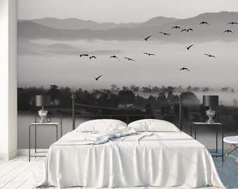May include: A white bed with a white duvet cover and a black metal frame. The bed is in front of a wall with a black and white photo mural of a misty mountain landscape with birds flying over it.