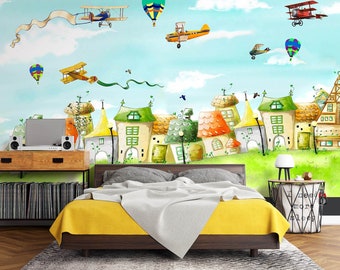May include: A yellow and white bed with a white comforter and a colorful cartoon mural on the wall behind it. The mural features houses, airplanes, and hot air balloons.