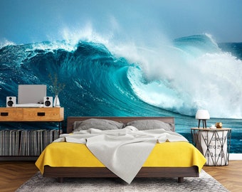 Puede incluir: Un dormitorio con una colcha amarilla y un gran mural de una ola de mar en la pared. La ola es de un azul y blanco vibrantes con una cresta espumosa. La cama está contra la pared y tiene una cabecera gris. Hay una pequeña mesita de noche con una lámpara y una cesta al lado de la cama.