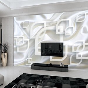 May include: A white wall with a modern abstract design featuring white geometric shapes and a white, flowing, silky texture. A black flat screen television is mounted on the wall. A black entertainment center with three drawers is below the television.