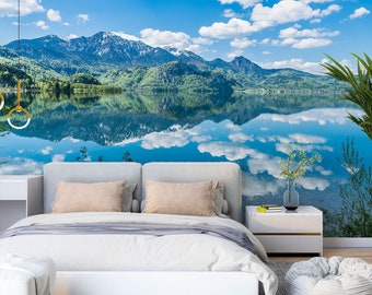 May include: A scenic mountain lake with a reflection of the sky and clouds in the water. The lake is surrounded by lush green trees and mountains in the background.