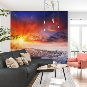 May include: A living room interior with a gray sectional sofa, a pink armchair, and a coffee table. The wall behind the sofa features a large mural of a colorful sunset over a body of water.