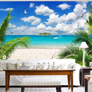 Puede incluir: Un sofá blanco con almohadas se encuentra frente a un mural de escena de playa tropical. El mural presenta palmeras, un cielo azul con nubes blancas y un océano turquesa con una pequeña isla en la distancia.