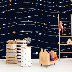 May include: A dark blue wall with white and yellow stars connected by white string lights. There are three storage baskets, a wooden toy box with a cat face, and a wooden ladder with a stuffed fox toy on the top rung.