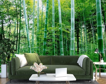 May include: A green velvet sofa with two pillows and a throw blanket sits in front of a photo mural of a lush bamboo forest. A white coffee table with a laptop and a vase of white flowers sits in front of the sofa.