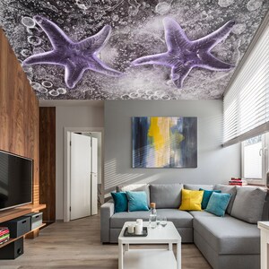 May include: A modern living room with a gray sectional sofa, white coffee table, and a large flat-screen TV. The ceiling features two purple starfish designs against a textured background. The room is decorated with colorful pillows and an abstract painting.
