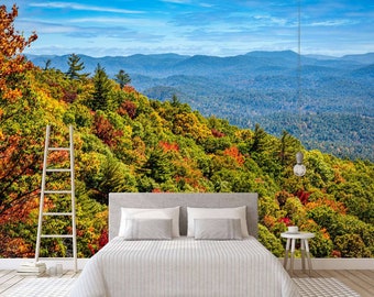 May include: A white bed with a white bedspread and two white pillows sits in front of a wall mural depicting a mountain range covered in autumn foliage. The foliage is a mix of green, yellow, orange, and red.