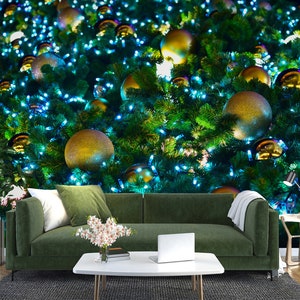 May include: A festive Christmas tree backdrop with gold ornaments and blue lights. A green sofa with white and green pillows, a white coffee table with a laptop, and a vase of flowers are in front of the tree.