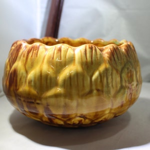 May include: A yellow ceramic planter with brown accents shaped like an artichoke.