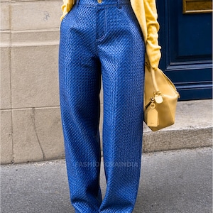 May include: Wide-leg, textured blue pants with a high waist. The pants are paired with a yellow sweater and a tan handbag. The shoes have a silver, sparkly toe. The text "FASHIONOVAINDIA" is visible on the pants.