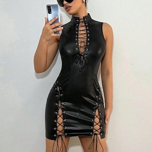 Puede incluir: Vestido negro sin mangas de cuero sintético con cuello alto y detalles de cordones en el corpiño y los laterales. El vestido es entallado y llega hasta la mitad del muslo.