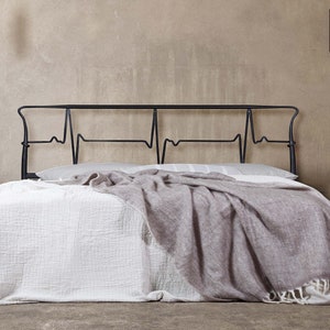 May include: A black metal bed frame with a headboard shaped like a heartbeat. The bed is made with white bedding and a gray throw blanket.