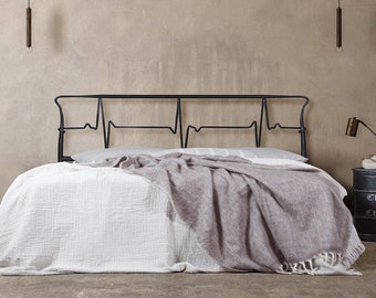 May include: A black metal bed frame with a headboard shaped like a heartbeat. The bed is made with white bedding and a gray throw blanket.