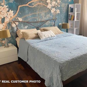 May include: A bedroom with a light blue bedspread and pillows. The headboard is metal, and the wall behind the bed has a floral mural. Two lamps sit on white nightstands. The text "REAL CUSTOMER PHOTO" is at the bottom.