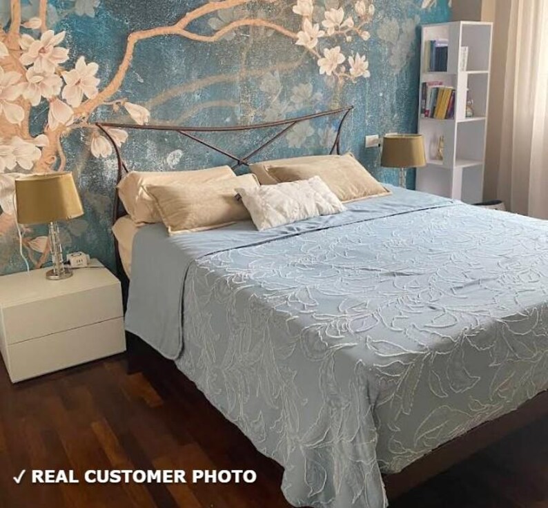 May include: A bedroom with a light blue bedspread and pillows. The headboard is metal, and the wall behind the bed has a floral mural. Two lamps sit on white nightstands. The text "REAL CUSTOMER PHOTO" is at the bottom.