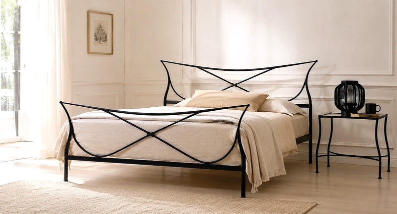 May include: Black metal bed frame with an arched headboard and footboard. The bed is made up with beige bedding and pillows. A small black side table with a lamp and a mug sits beside the bed. The room has a neutral color palette.