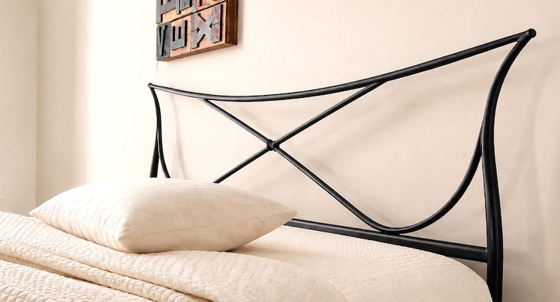 May include: Black metal bed headboard with a curved design. The headboard has an X-shaped detail in the center and is positioned above a bed with a cream-colored pillow and bedding. A decorative wooden piece hangs on the wall.