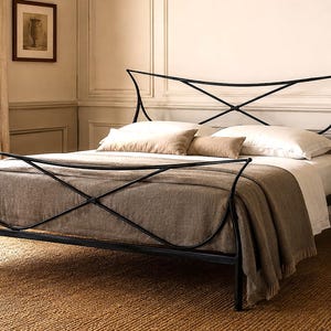 May include: A black metal bed frame with an X-shaped design on the headboard and footboard. The bed is made up with white sheets, pillows, and a brown blanket. A woven rug is on the floor.