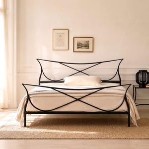 May include: A black metal bed frame with a unique, curved design. The bed is made up with a cream-colored comforter and pillows. The room has a neutral color palette, with a rug, side table, and a potted plant. The bed frame is approximately 78 inches long.