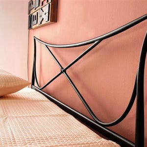 May include: Black metal bed frame headboard with an arched design. The headboard has a decorative X-shaped detail in the center. A peach-colored pillow and bedspread are visible. The headboard is against a peach-colored wall.