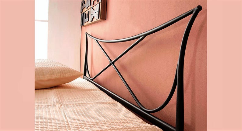May include: Black metal bed frame headboard with an arched design. The headboard has a decorative X-shaped detail in the center. A peach-colored pillow and bedspread are visible. The headboard is against a peach-colored wall.