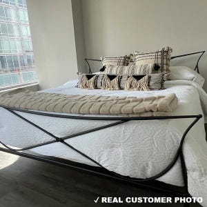 May include: A bed with a black metal frame, white bedding, and decorative pillows. The pillows have black and white patterns and fringe. A beige textured throw blanket is at the foot of the bed. The text "REAL CUSTOMER PHOTO" is at the bottom.