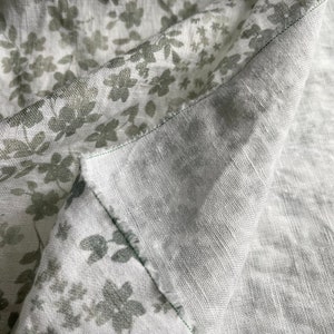 May include: Close-up of two pieces of fabric, one with a light gray background and a subtle green floral pattern, and the other a solid light gray. The fabrics are folded over each other, showing the seam where they are sewn together.