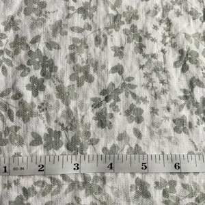 May include: White fabric with a gray floral pattern. A measuring tape is placed on the fabric, showing measurements in inches.