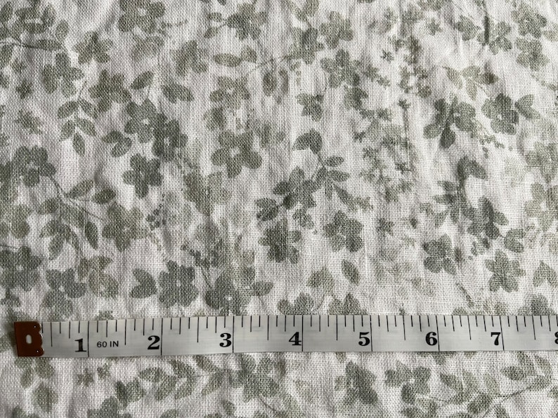 May include: White fabric with a gray floral pattern. A measuring tape is placed on the fabric, showing measurements in inches.