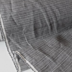 May include: A roll of gray fabric with a subtle striped pattern. The fabric has a textured appearance with a light sheen, and a white border runs along the edge. The material appears to be a woven textile, suitable for various sewing projects.
