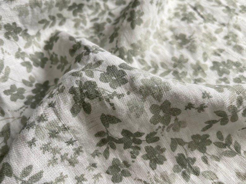 May include: White fabric with a subtle green floral pattern. The fabric has a linen texture and a soft, drapey feel.