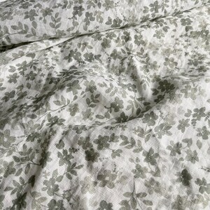 May include: White linen fabric with a gray floral pattern. The fabric is wrinkled and has a soft, textured feel.