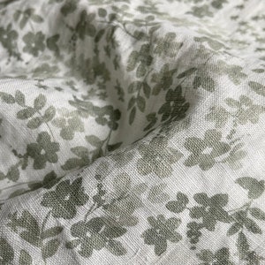 May include: White fabric with a subtle green floral pattern. The fabric has a linen texture.