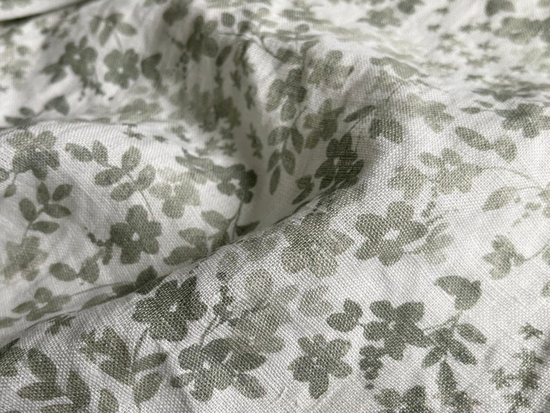 May include: White fabric with a subtle green floral pattern. The fabric has a linen texture.