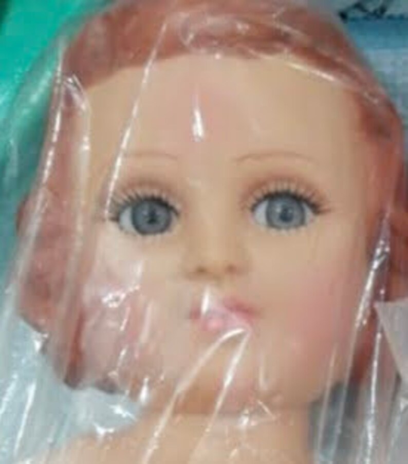 May include: A close-up of a doll head with long, straight, auburn hair. The doll has blue eyes and a painted, realistic face.