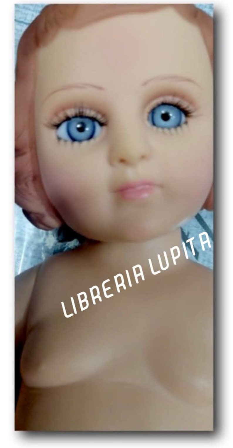 May include: A close-up of a doll's face with blue eyes and a light pink mouth. The doll is wearing a white dress and has the text "LIBRERIA LUPITA" printed on its chest.