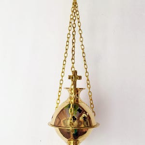 May include: A gold-colored censer, suspended by chains, with a cross on top. The censer has a round body with decorative cutouts and a flared base. The chains connect to a ring at the top.