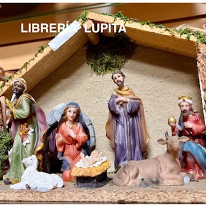 May include: A Nativity scene with figurines of Mary, Joseph, baby Jesus, the Three Wise Men, and a lamb. The figures are in various colors, including red, purple, and green, and are set inside a wooden stable. The text "Librería Lupita" is at the top.
