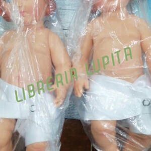 May include: Two plastic baby dolls wrapped in clear plastic bags. The dolls are nude and wearing white cloth diapers. The dolls are posed with their arms outstretched. The dolls are labeled "Libreria Lupita".