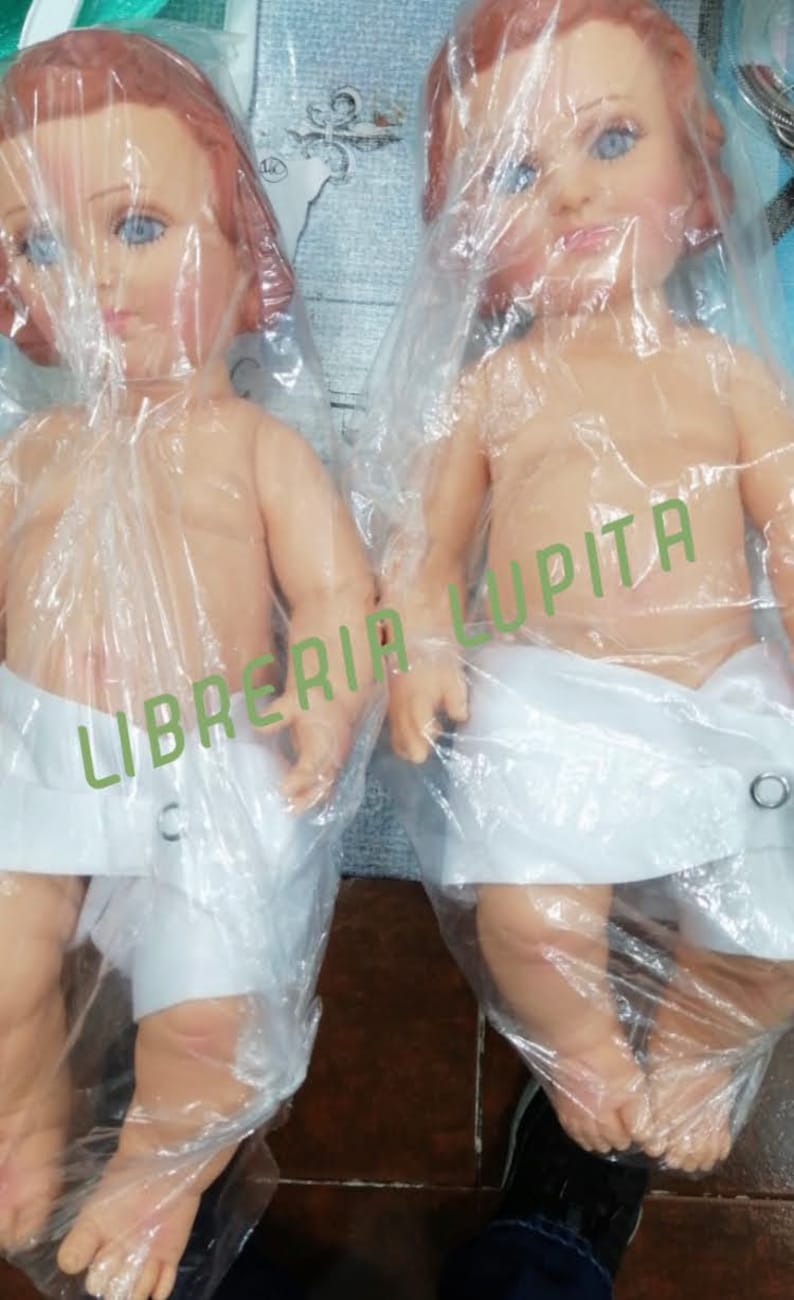 May include: Two plastic baby dolls wrapped in clear plastic bags. The dolls are nude and wearing white cloth diapers. The dolls are posed with their arms outstretched. The dolls are labeled "Libreria Lupita".