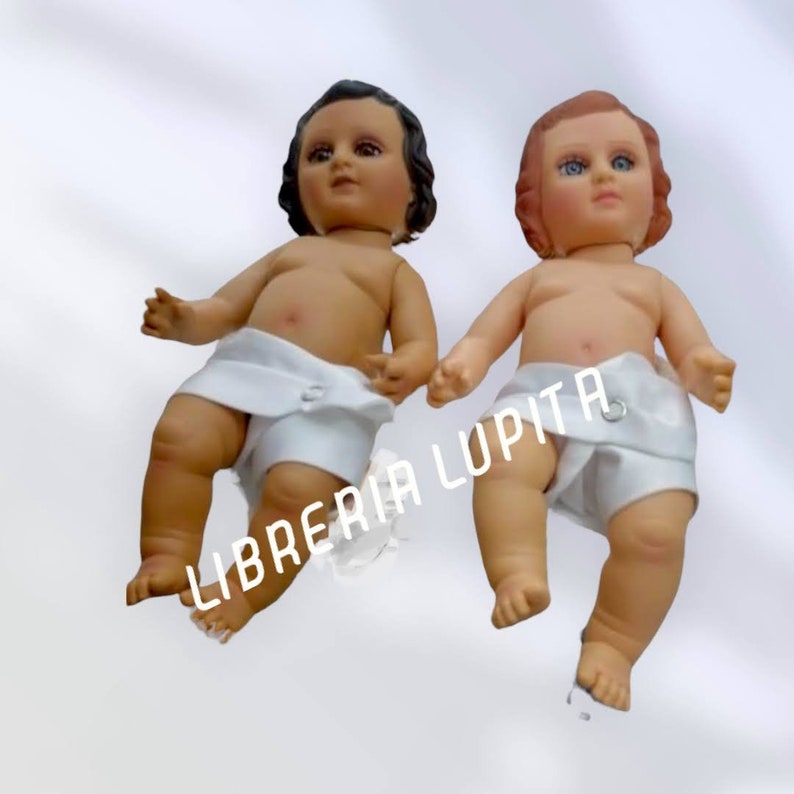 May include: Two baby dolls dressed in white cloth diapers. The dolls have realistic features and are posed in a sitting position. The dolls are on a white background. The text "LIBRERIA LUPITA" is visible in the image.