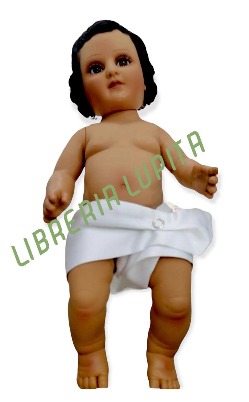 May include: A small, white-clothed doll with dark hair and a painted face. The doll is standing with its legs slightly apart and its arms outstretched.