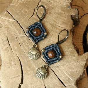 Peut inclure: Une paire de boucles d'oreilles noires et brunes avec un charme en forme de coquille. Les boucles d'oreilles sont faites avec un cordon noir et une pierre œil de tigre brune.