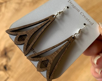 Puede incluir: Un par de pendientes de madera marrón con un diseño floral. Los pendientes están en una tarjeta blanca con el texto "Dragon Created" impreso en ella.